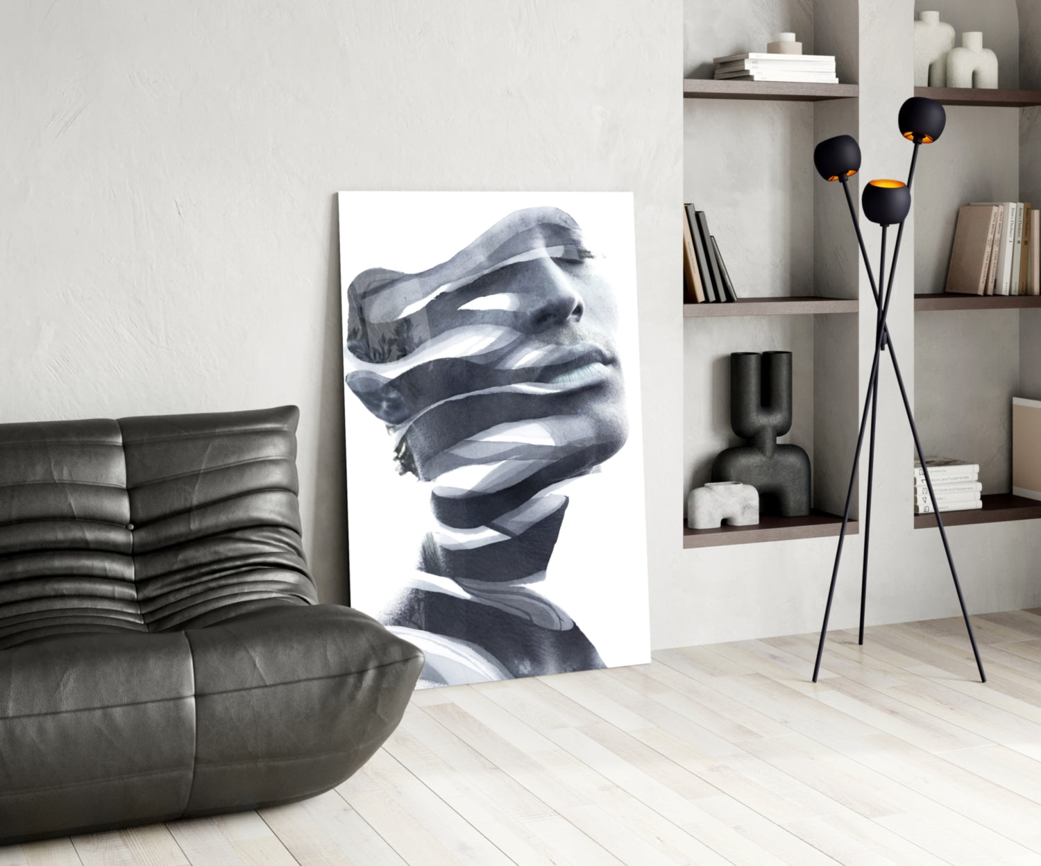 Modern living room interior with black and white portrait glass art leaning against wall beside gray sofa.