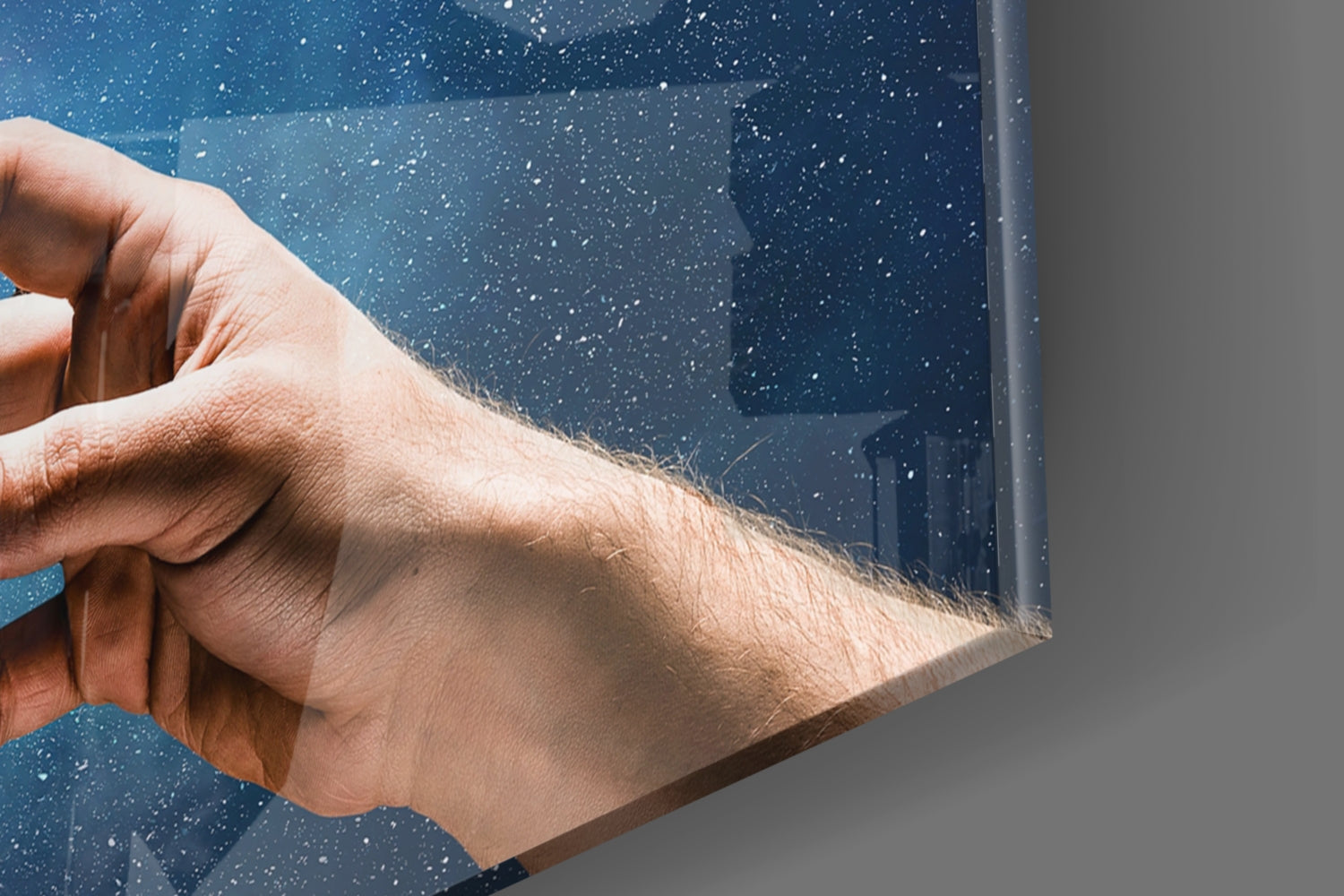 Hand holding blue speckled glass panel at an angle, showing water droplets and reflective surface detail.