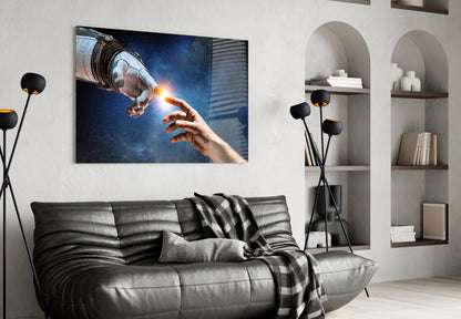 Creation Glass Wall Art depicting two hands touching with glowing light, displayed above a gray leather sofa in a modern living room.