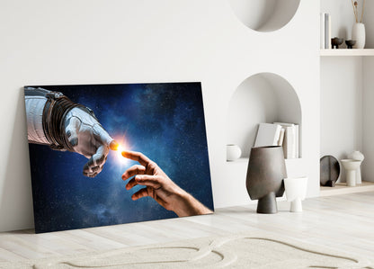 Creation glass wall art leaning against white wall shows astronaut and human hand touching with glowing light against starry blue space background.