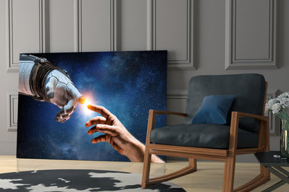 Creation Glass Wall Art displaying an astronaut and human hand touching against a starry blue cosmic background, installed in a modern living room setting.