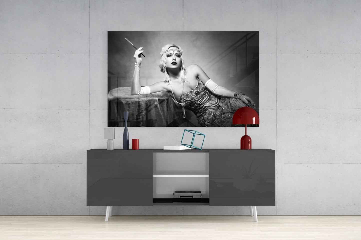 Black and white vintage-style glass wall art depicting a 1920s woman with cigarette holder displayed above gray media console with red accents.