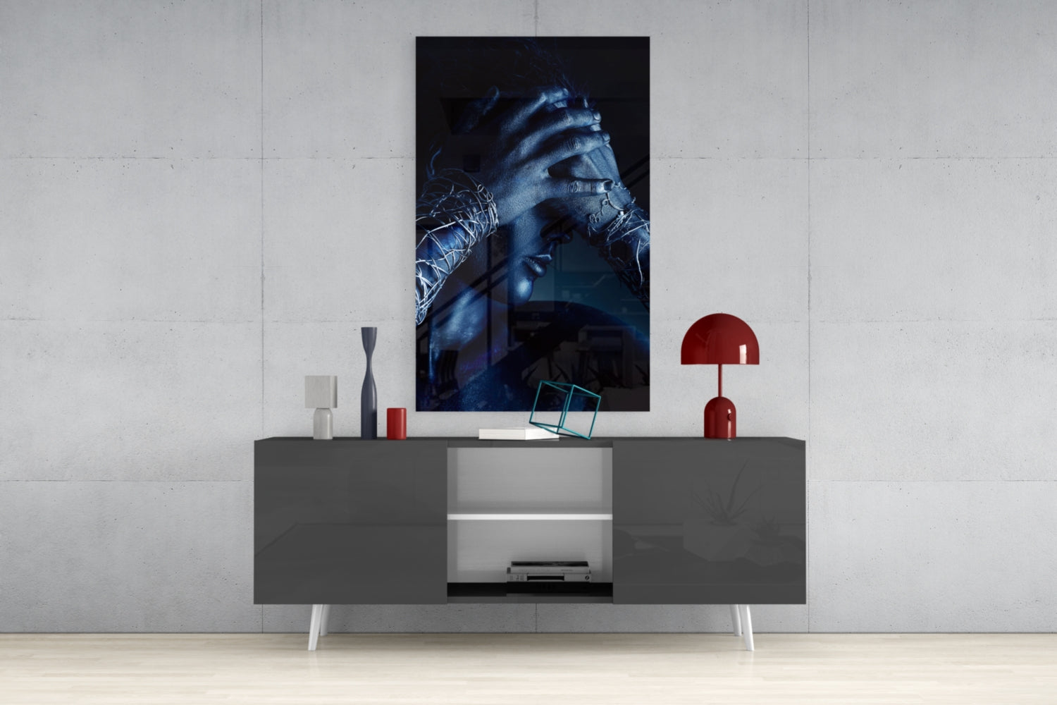 Deep Thought Glass Wall Art displayed above a dark gray media console, showing blue-toned portrait of hands with decorative objects and red lamp nearby.