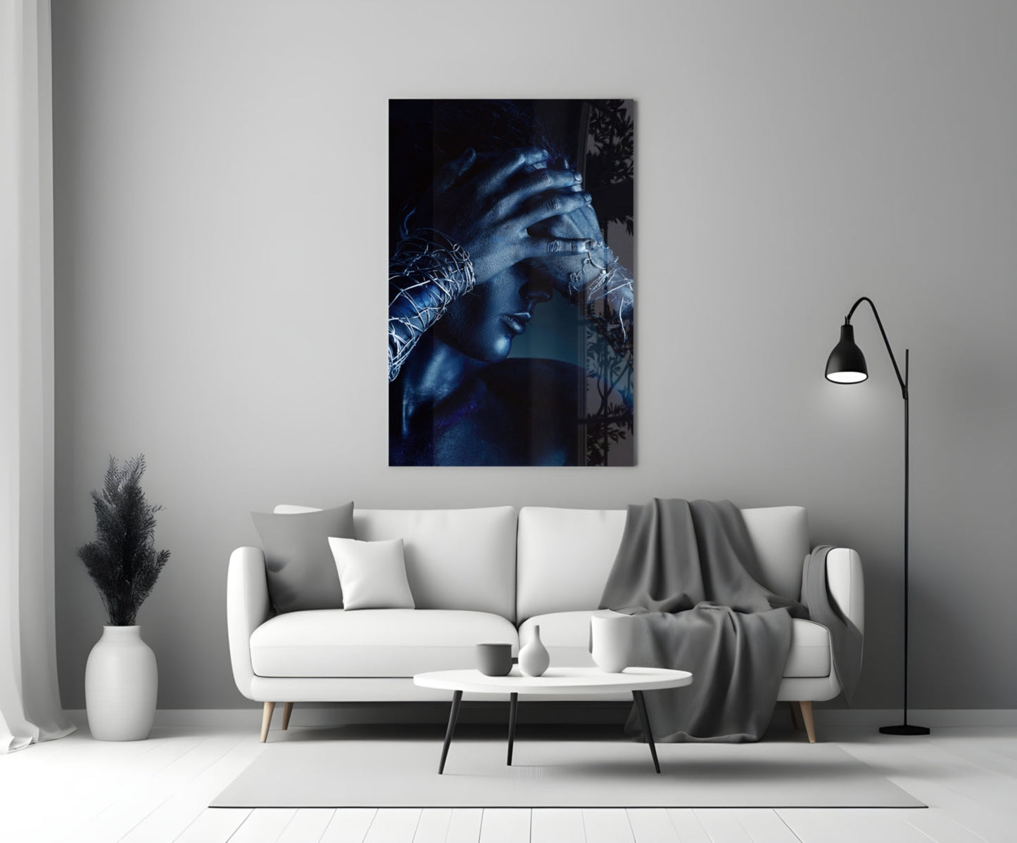 Deep Thought Glass Wall Art displaying a blue-toned portrait of a contemplative figure with hand to face, hung above a white sofa in a minimalist interior.