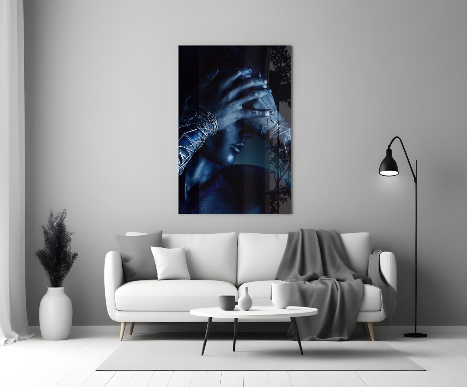 Deep Thought Glass Wall Art displaying a blue-toned portrait of a contemplative figure with hand to face, hung above a white sofa in a minimalist interior.