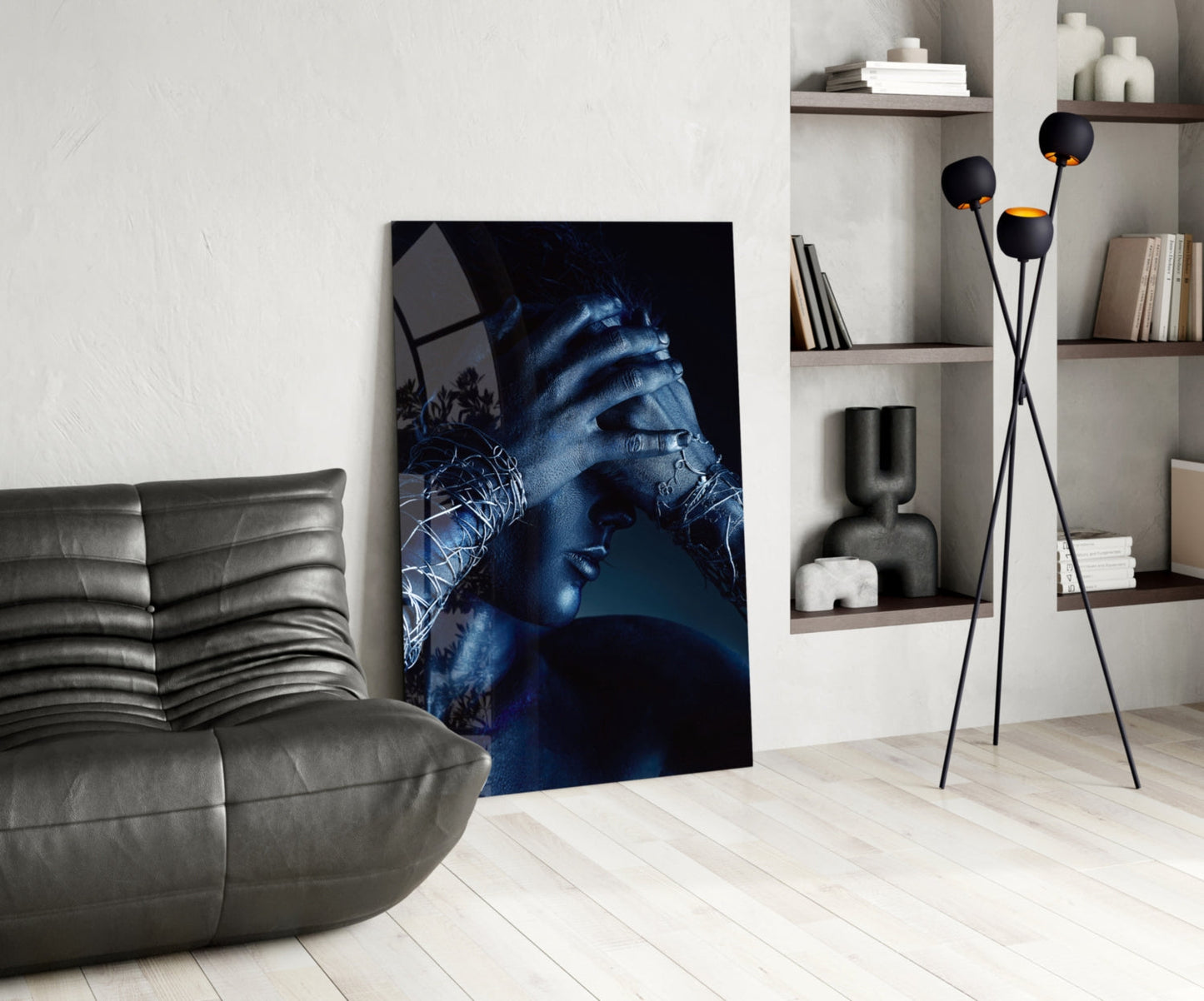 Modern living room interior featuring Deep Thought glass wall art displaying blue-toned portrait with hands, positioned beside gray leather chair and shelving unit.