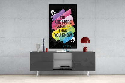 Motivational glass wall art with colorful paint strokes and text "You Are More Capable Than You Know" displayed above gray media console in modern interior.