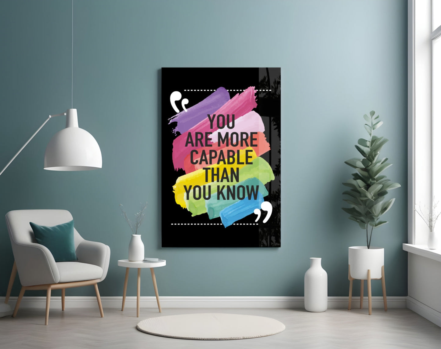 Motivational glass wall art with colorful brush strokes and black text displayed in a modern room with teal walls, white furniture, and plants.