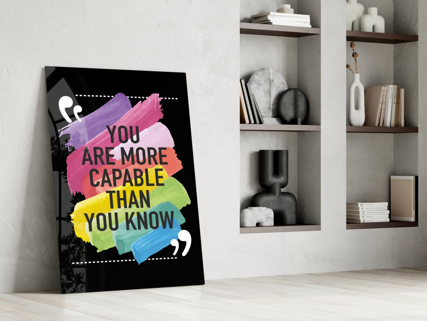 Motivational glass art leaning against white wall displays colorful brush strokes and black text reading "You Are More Capable Than You Know" beside built-in shelving.