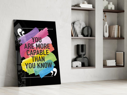 Motivational glass art leaning against white wall displays colorful brush strokes and black text reading "You Are More Capable Than You Know" beside built-in shelving.