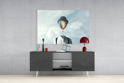 Glass wall art depicting surreal figure with hot air balloon head displayed above gray console table in modern interior.