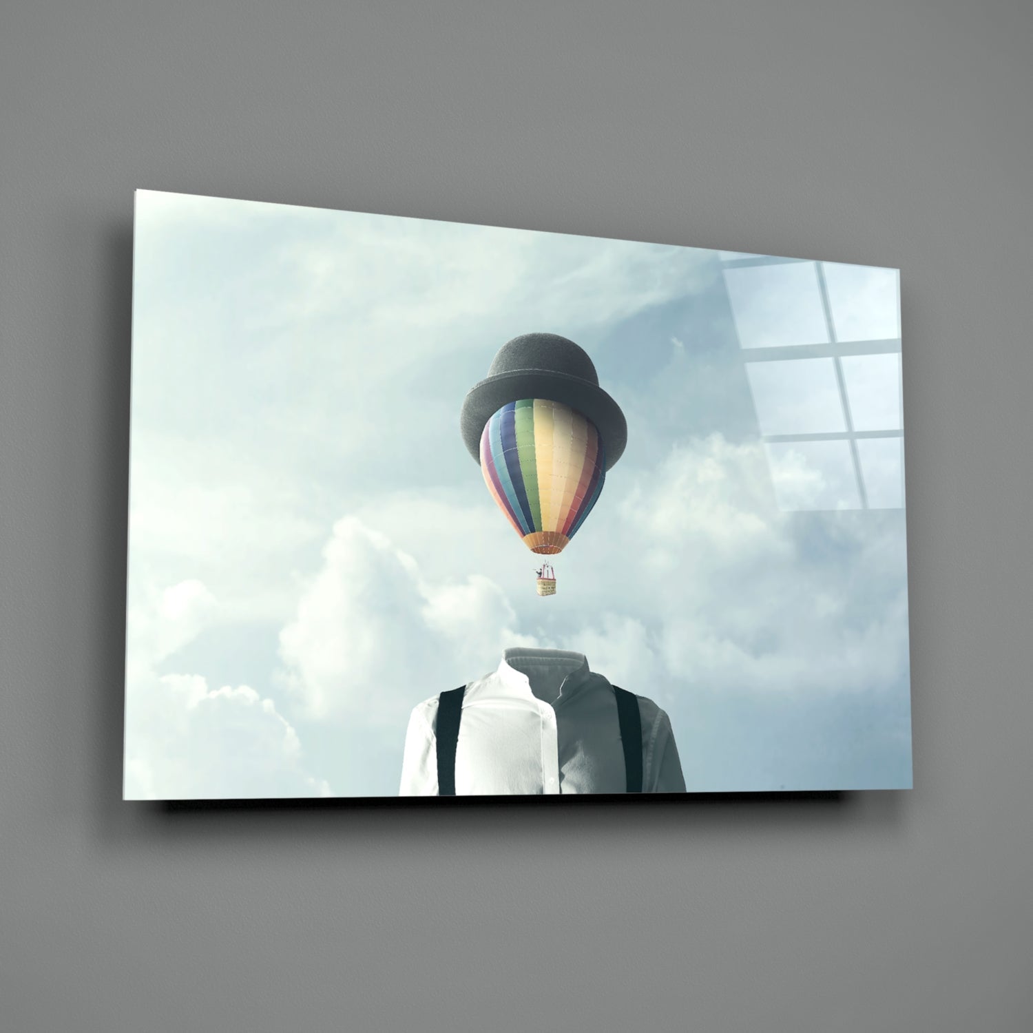 Glass wall art displaying a figure in formal attire with a colorful hot air balloon replacing the head against a cloudy sky.