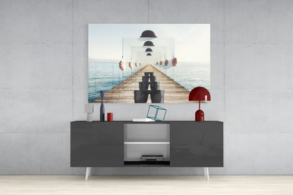 Surreal glass wall art depicting a recursive pier with bowler hats displayed above a dark media console with red lamps and decorative objects.