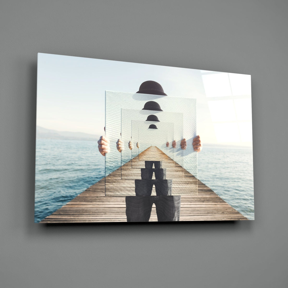 Surreal glass wall art displaying a wooden pier extending toward ocean with recursive silhouettes of bowler hats and seated figures in diminishing perspective.