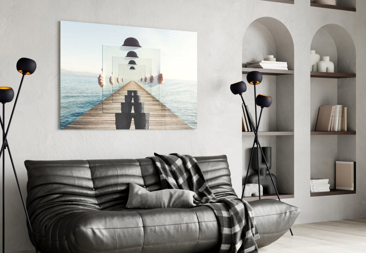 Surreal recursive pier artwork displayed on white wall above black leather sofa with bookshelves and decorative black flowers nearby.