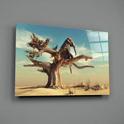 Glass wall art mounted on gray wall showing elephant balancing on gnarled tree in desert landscape under blue sky.