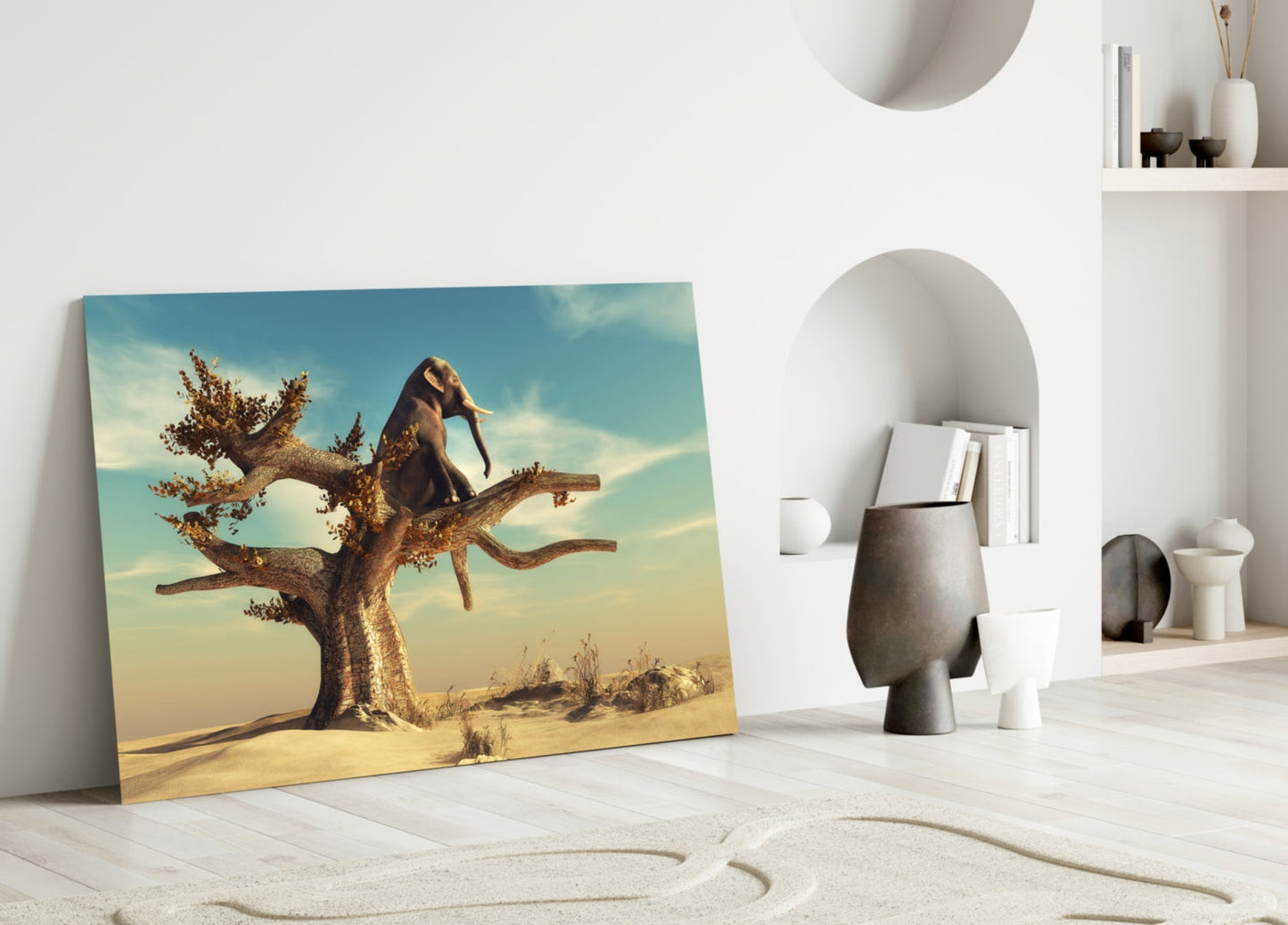 Glass wall art leaning against white wall displays elephant balancing on golden tree branch in desert landscape with blue sky.