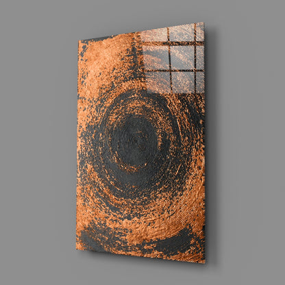 Angled perspective view of glass wall art featuring concentric copper and black spiral design against gray background.