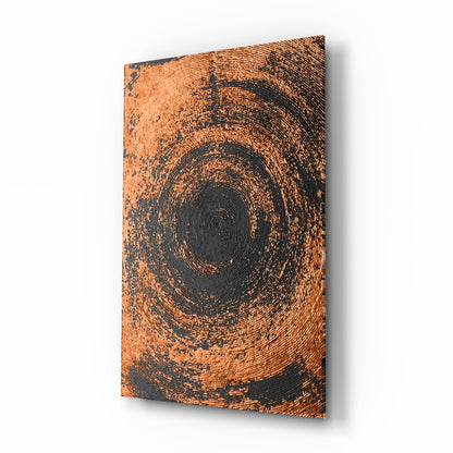 Angled view of rectangular glass wall art with concentric copper and dark gray spiral pattern, displayed against white background.