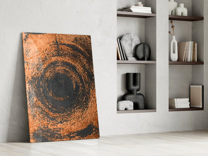 Copper spiral swirl glass wall art leaning against white wall beside built-in shelving with decorative objects.