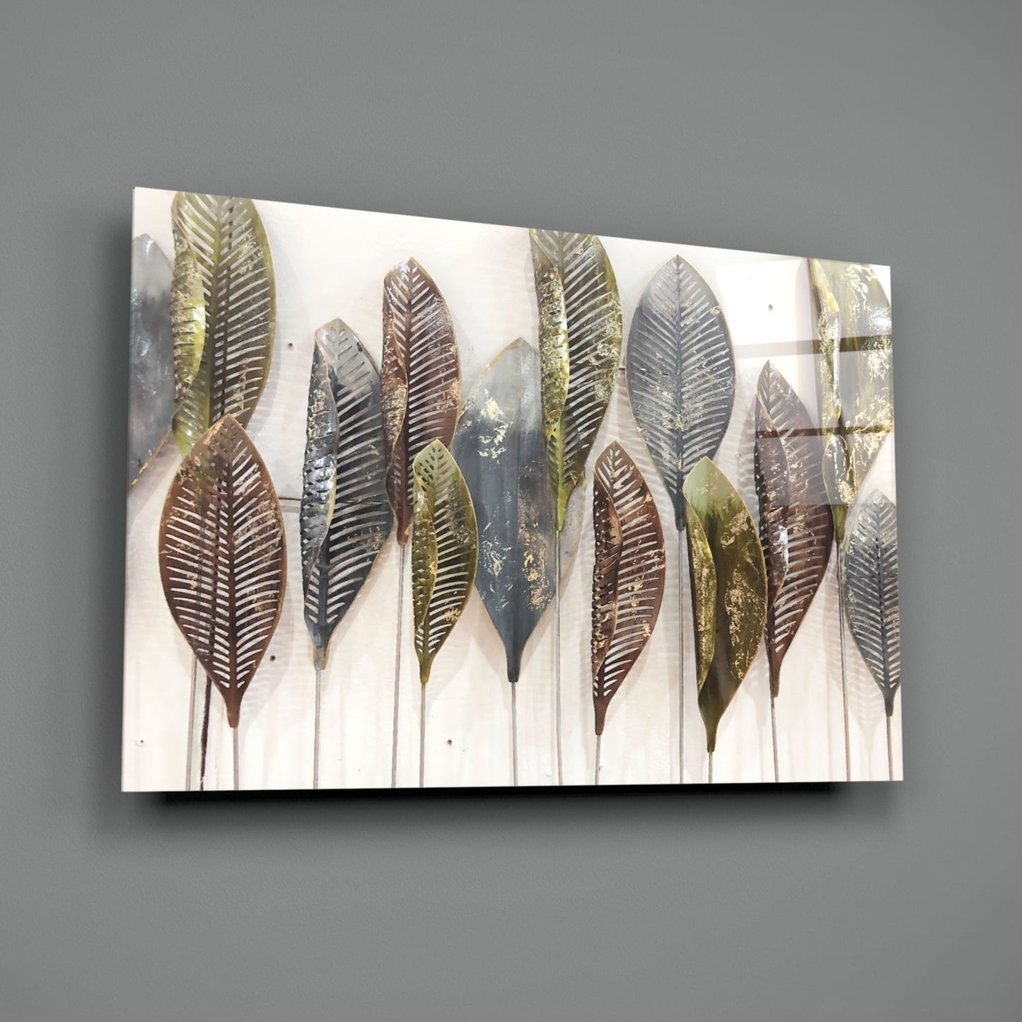 Angled view of glass wall art displaying metallic feather designs in gold, bronze, and silver tones on cream background, mounted on gray wall.