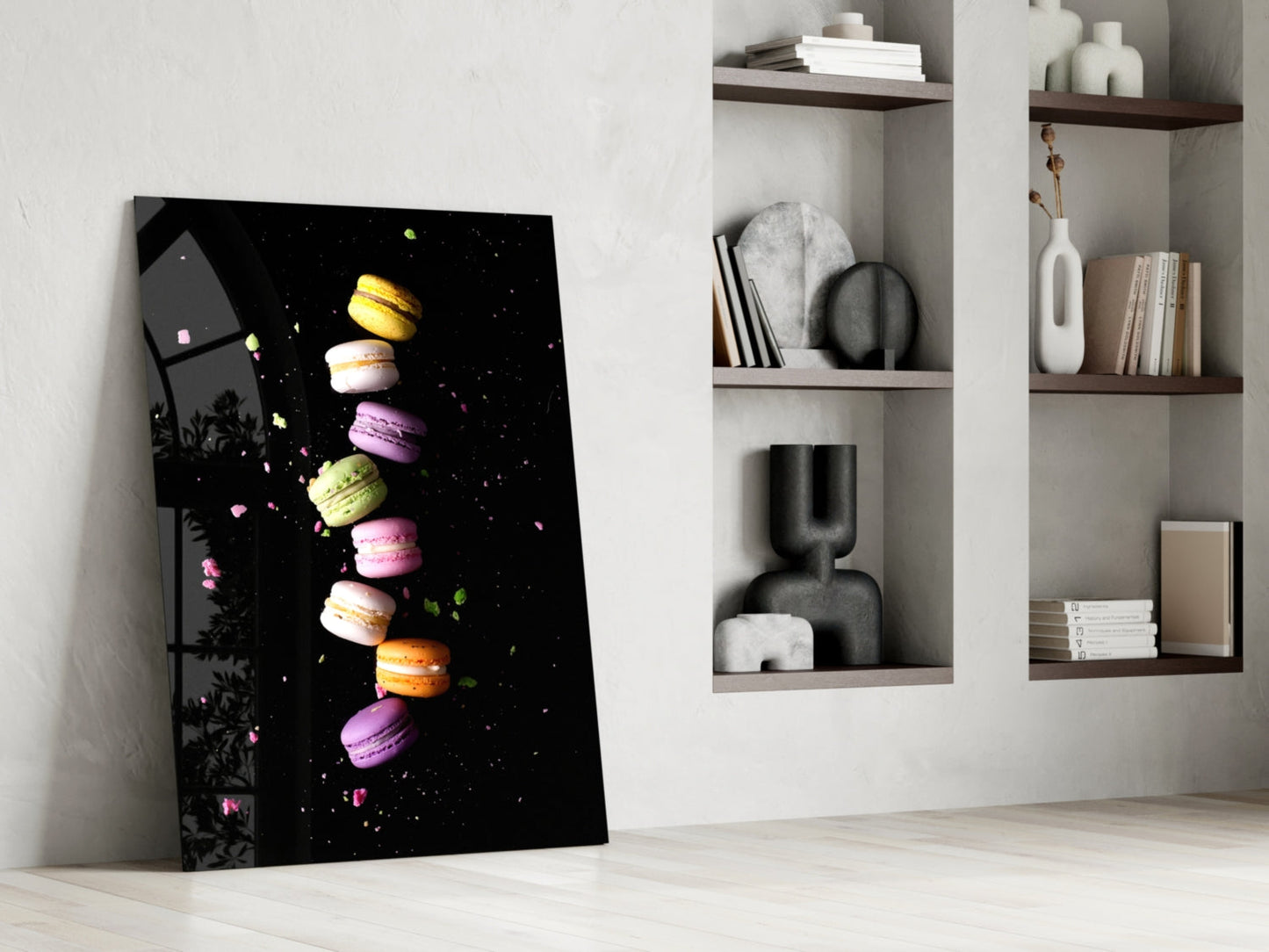 Colorful macarons stacked vertically on black glass art leaning against white wall beside wooden shelves.