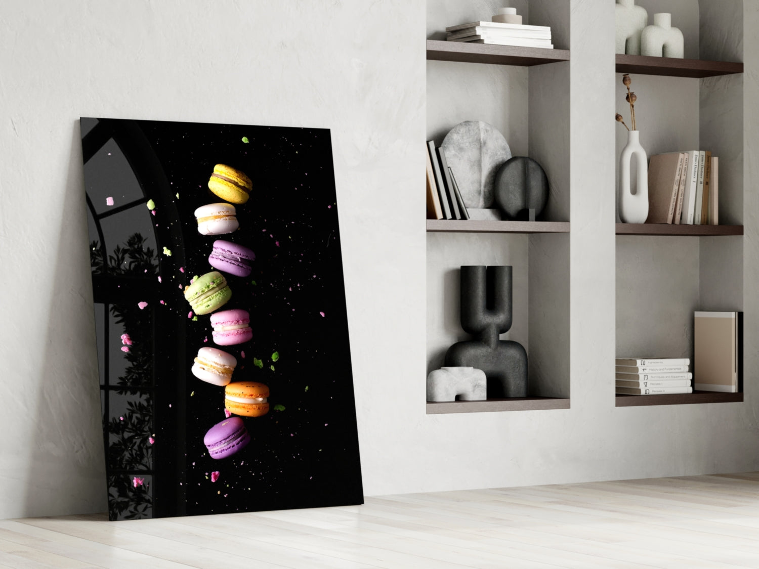 Colorful macarons stacked vertically on black glass art leaning against white wall beside wooden shelves.