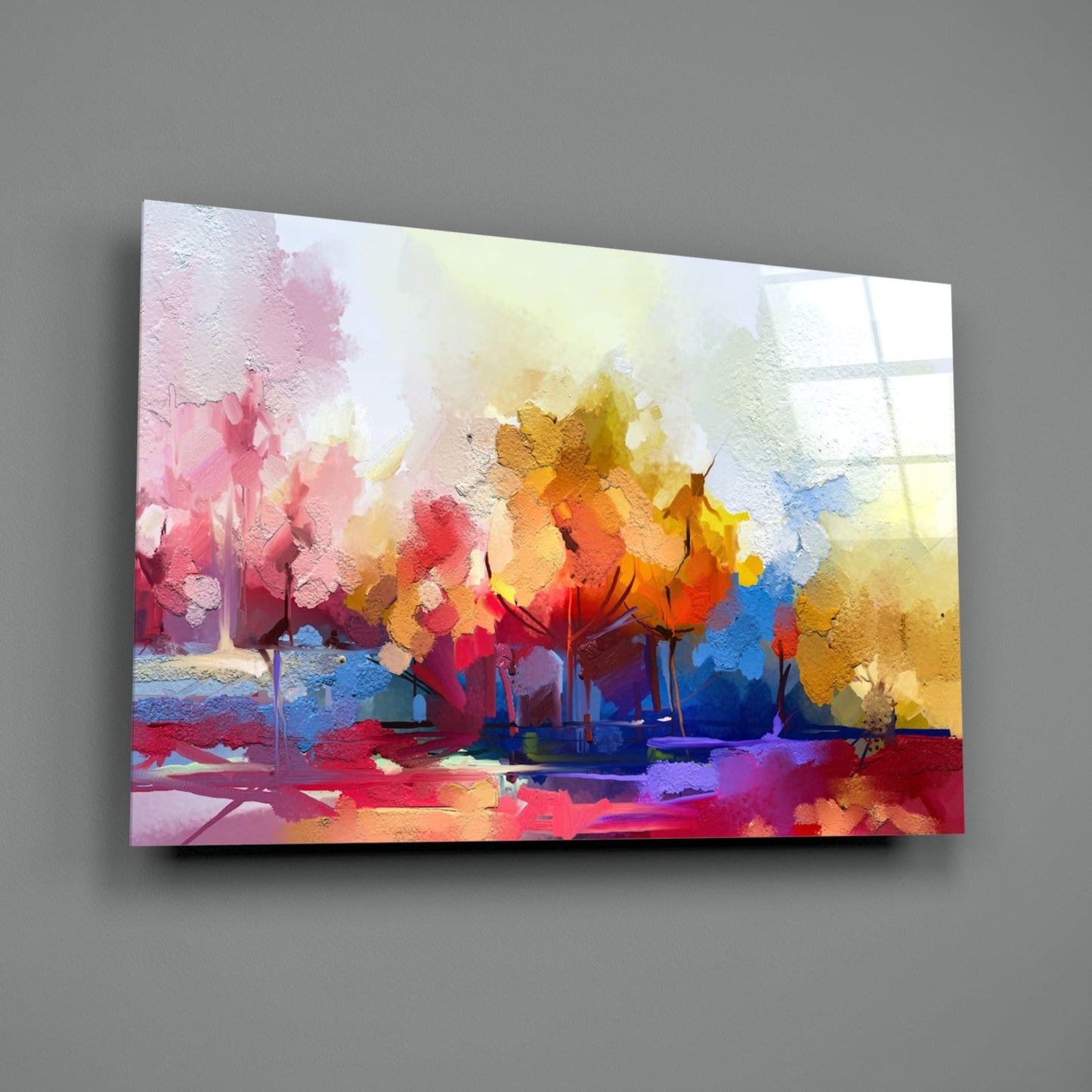 Angled view of colorful abstract tree glass wall art with vibrant pink, yellow, orange, and blue watercolor-style brushstrokes on gray wall.