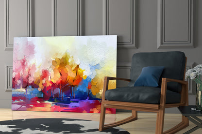 Colorful abstract trees glass wall art displayed in a modern living room next to a wooden rocking chair with black cushions.