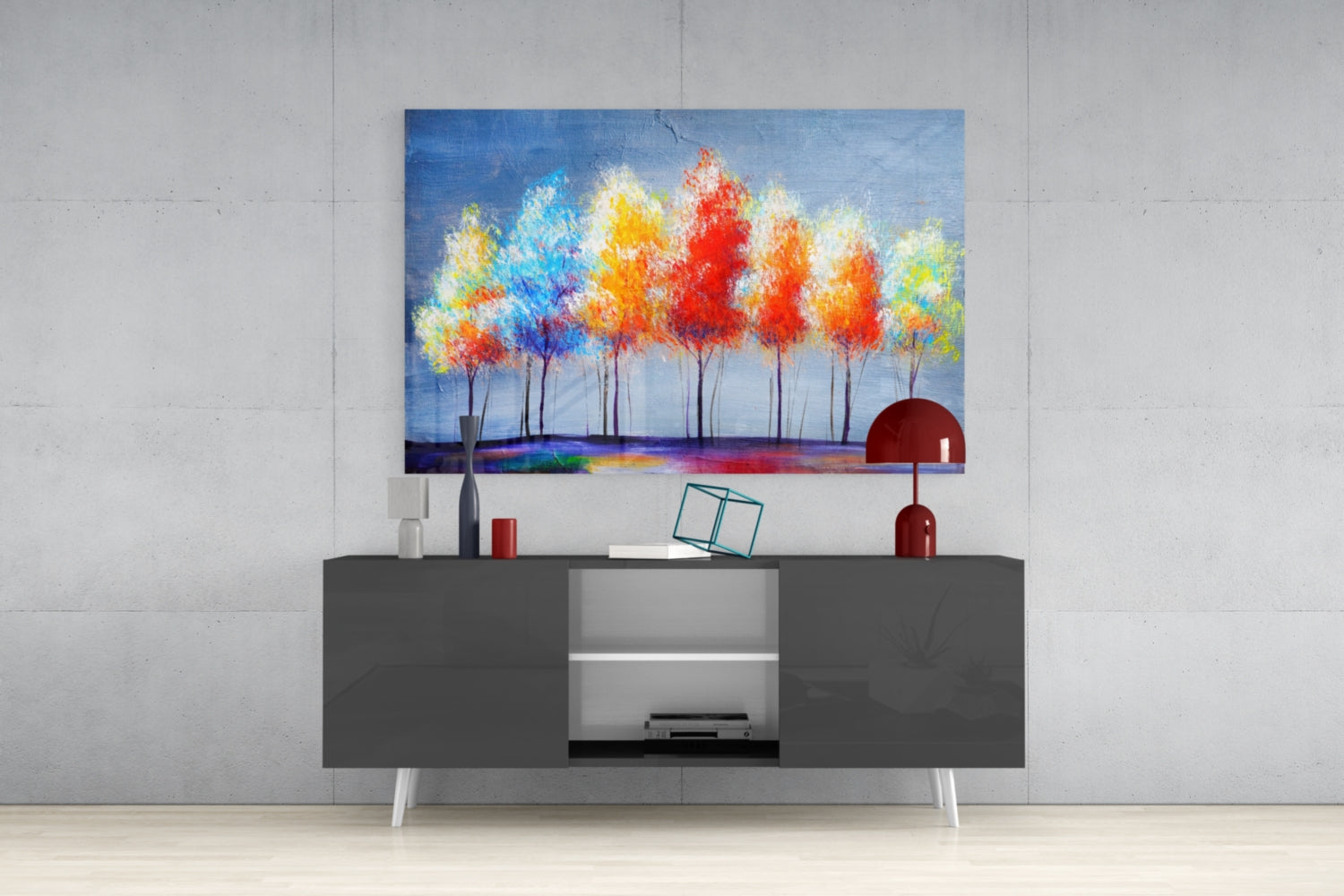 Colorful glass wall art depicting vibrant trees in reds, yellows, and blues displayed above a dark gray media console in a modern interior setting.