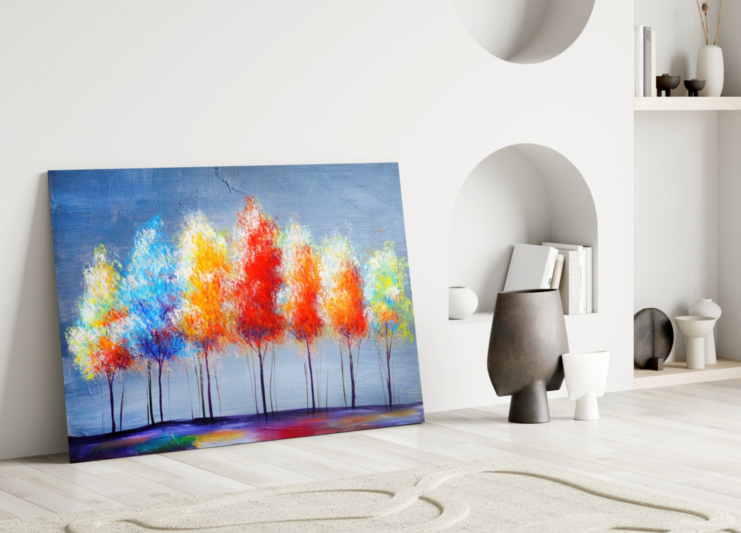 Colorful glass wall art leaning against white wall displaying vibrant red, orange, yellow trees on blue background in minimalist interior setting.