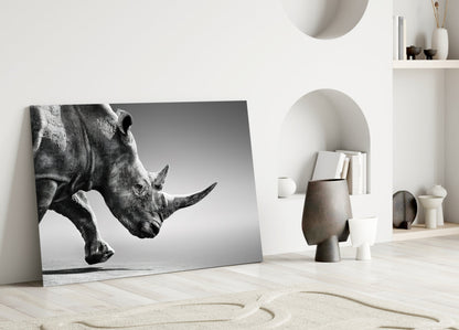 Black and white rhino portrait glass wall art leaning against white wall in minimalist interior setting.