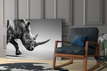 Black and white glass wall art featuring a rhino in profile, displayed in a modern living room next to a wooden chair.