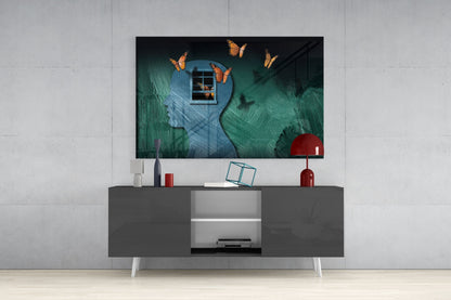 Surreal glass wall art depicting teal and blue profile heads with orange butterflies, displayed above a modern gray TV console in a living room setting.