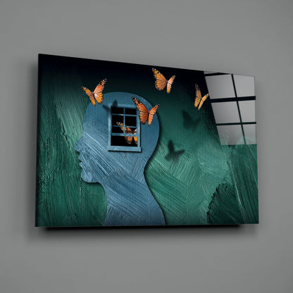 Glass wall art displaying a blue silhouetted head with window and orange butterflies against green textured background.