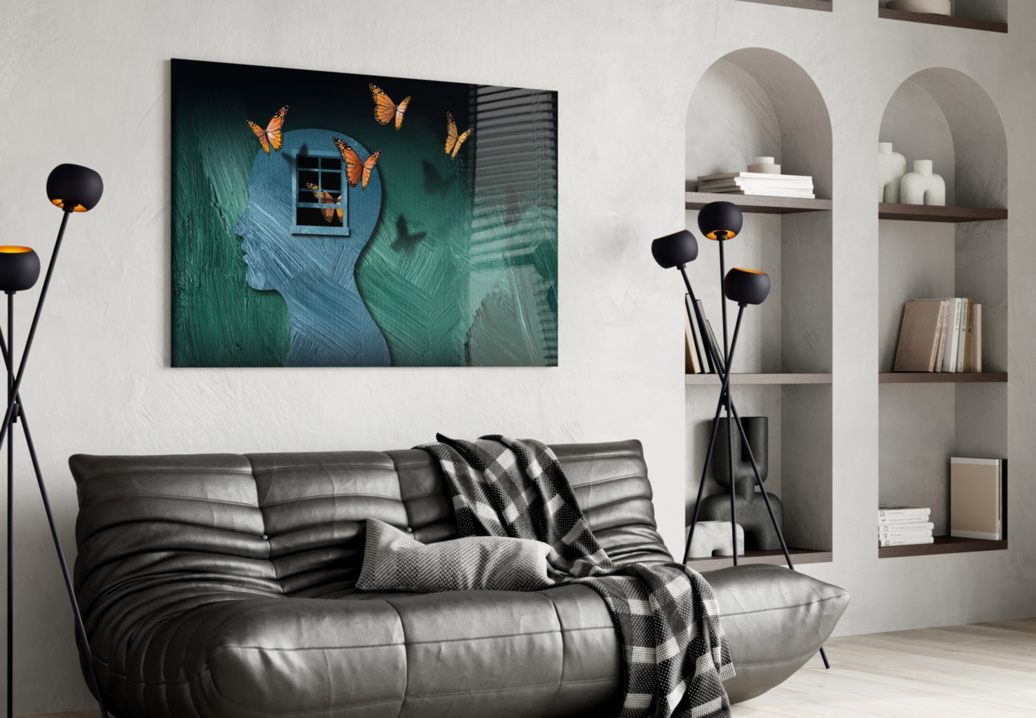 Glass wall art displaying a teal textured head silhouette with orange butterflies and a window, hung above a black leather sofa in a modern living room.
