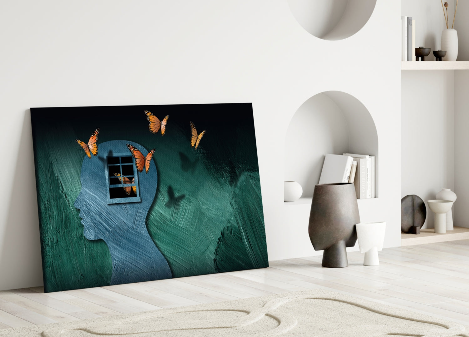 Glass wall art leaning against white wall displays blue silhouette head with window and orange butterflies on teal background.