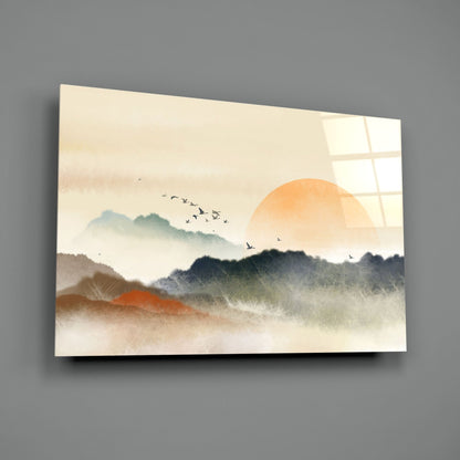 Glass wall art displaying misty layered mountains in grey and orange tones with a large sun and flying birds against a cream background.