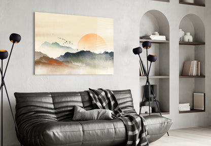 Abstract landscape glass wall art depicting misty mountains and orange sun displayed above black leather sofa in modern living room.