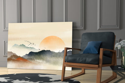 Abstract landscape glass wall art depicting misty mountains and orange sun displayed in modern living room setting with wooden chair.