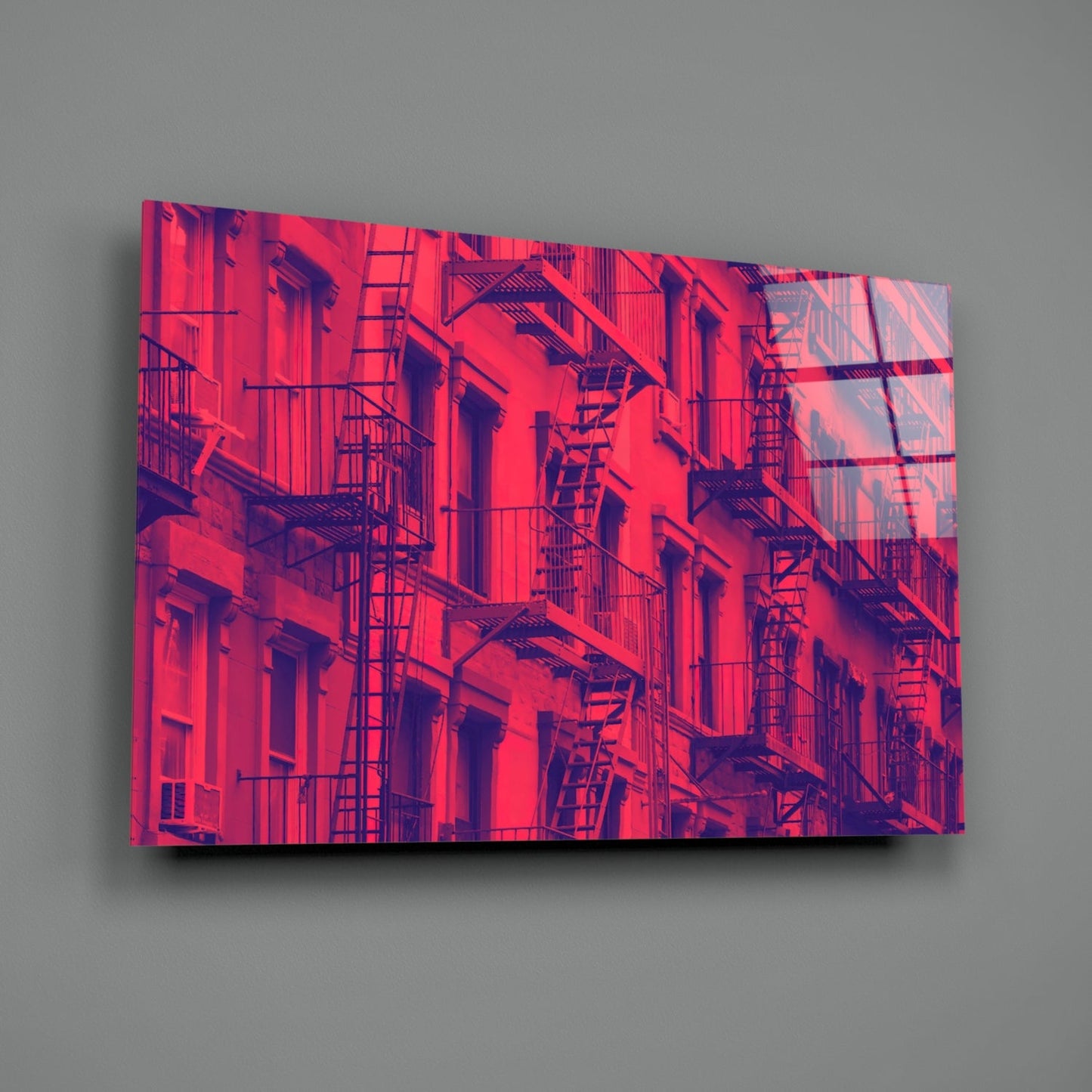 Neon pink and purple tinted glass wall art depicting a building facade with fire escapes and windows, mounted on gray wall.