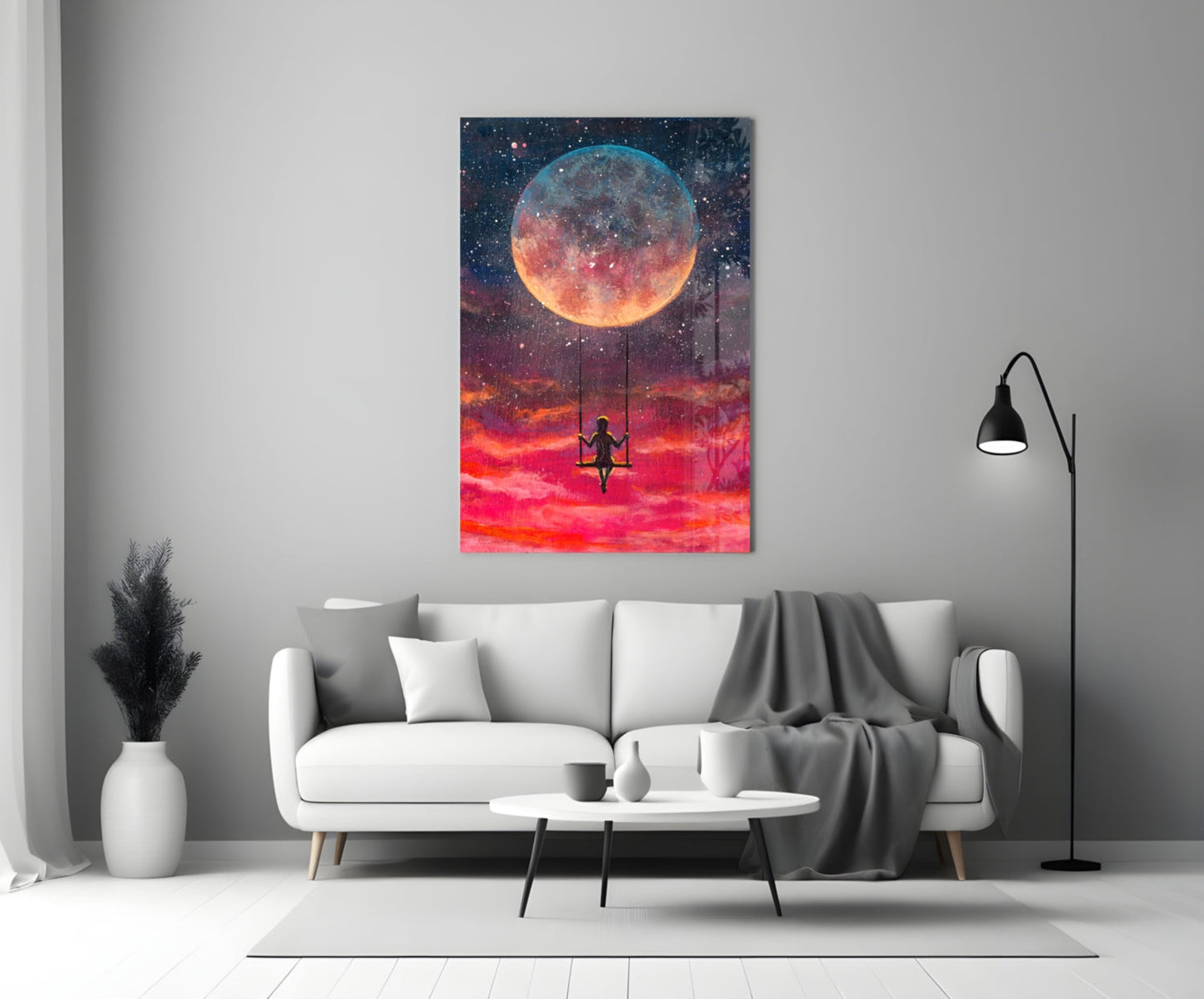 Freedom Glass Wall Art displaying a silhouetted figure on a swing beneath a large glowing moon in a vibrant red and orange sky, hung above a white sofa in a modern living room.