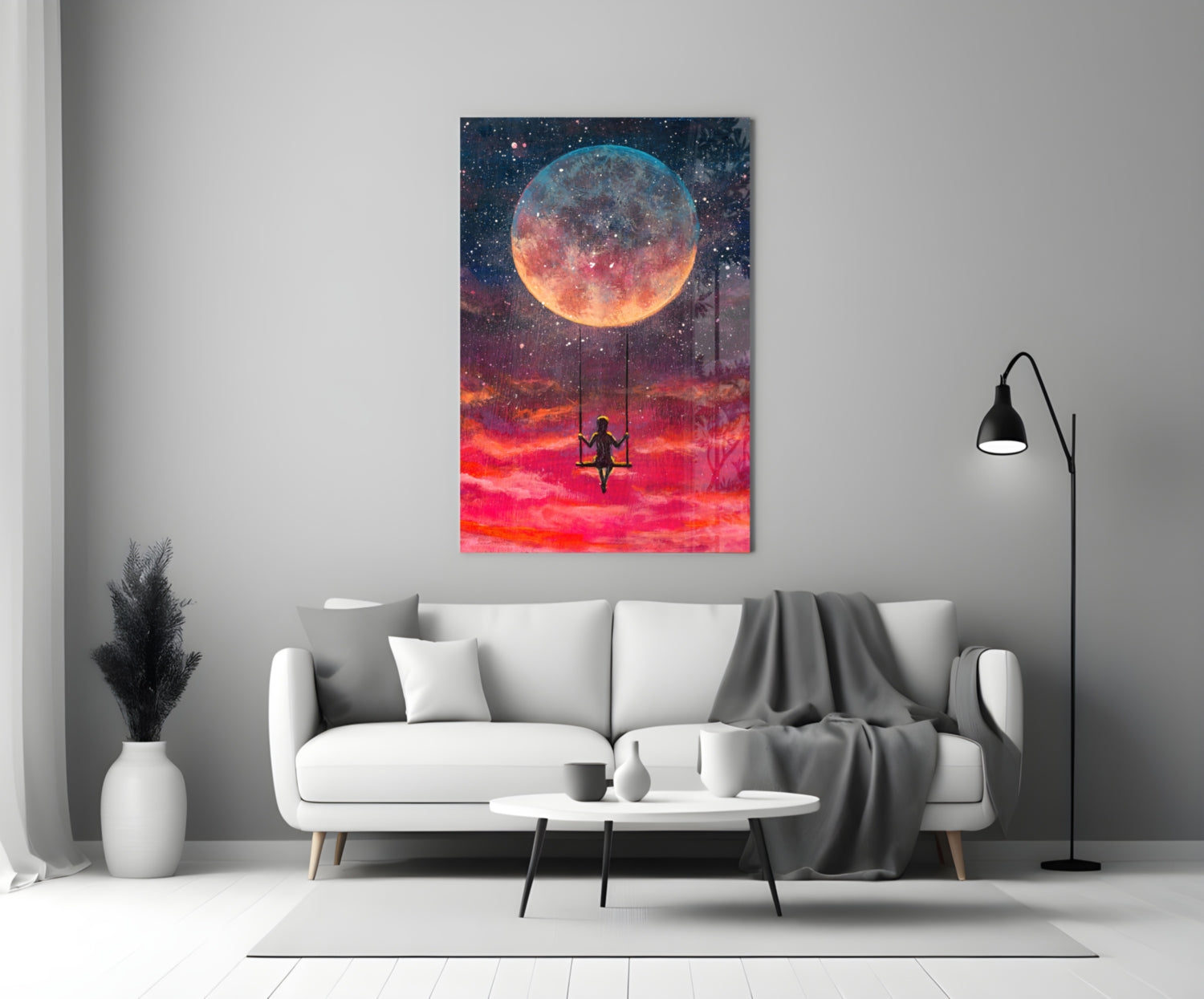 Freedom Glass Wall Art displaying a silhouetted figure on a swing beneath a large glowing moon in a vibrant red and orange sky, hung above a white sofa in a modern living room.