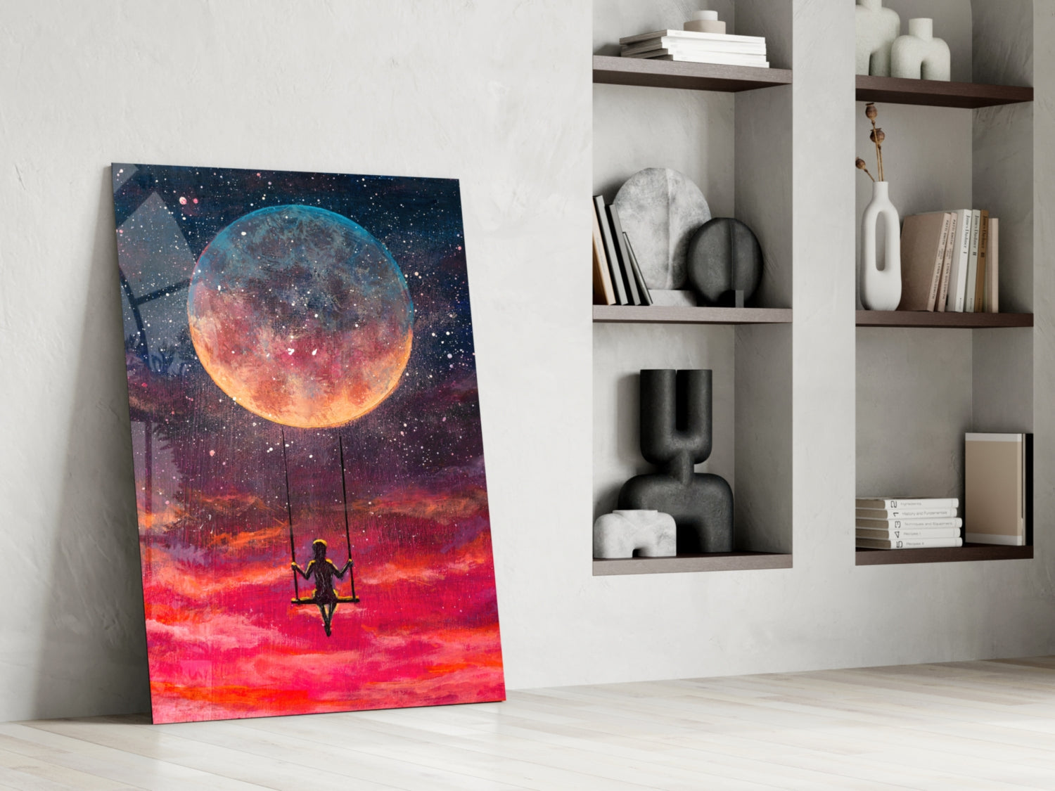 Canvas art leaning against white wall displays silhouetted figure on swing beneath glowing moon and fiery red sky with stars.