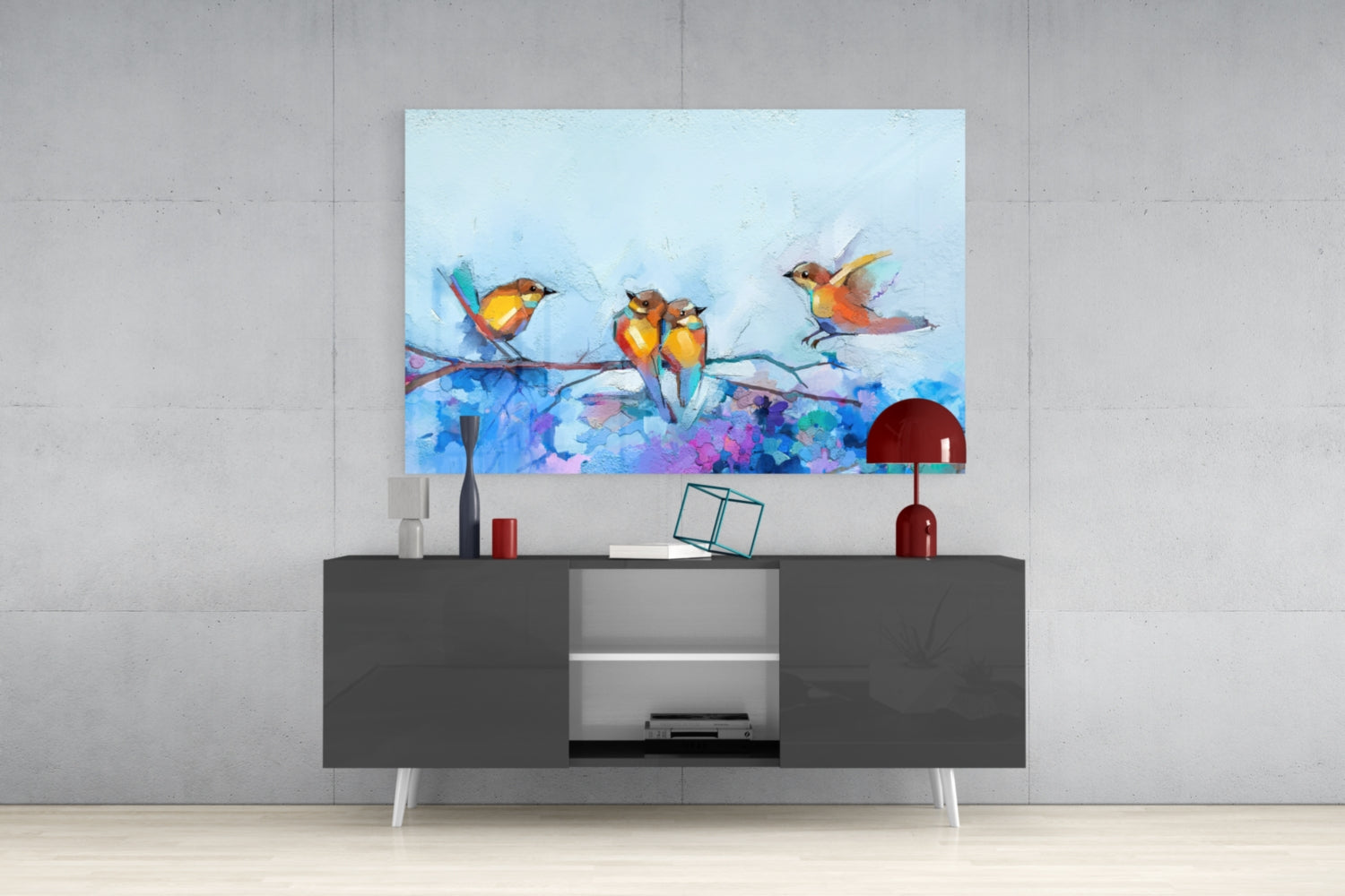 Colorful glass wall art featuring four orange and yellow birds perched on a branch above purple and blue watercolor flowers, displayed above a dark gray media console.