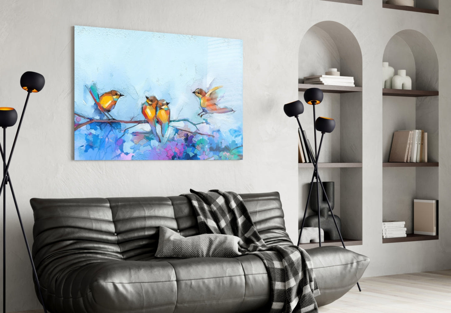 Colorful glass wall art depicting three painted birds on a branch above vibrant blue and purple watercolor splashes, displayed above a black leather sofa in a modern living room.