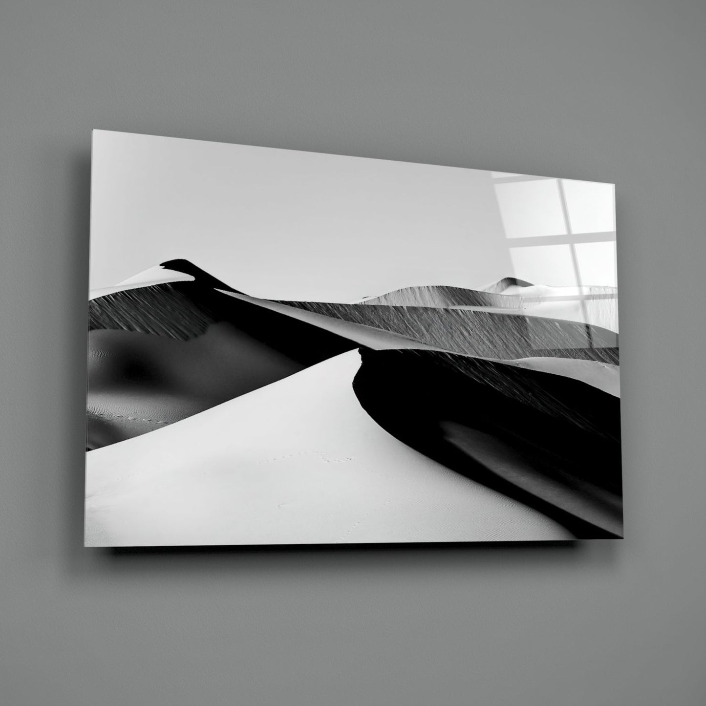 Black and white glass wall art mounted on gray wall, displaying abstract sand dunes with strong shadows and contrast.