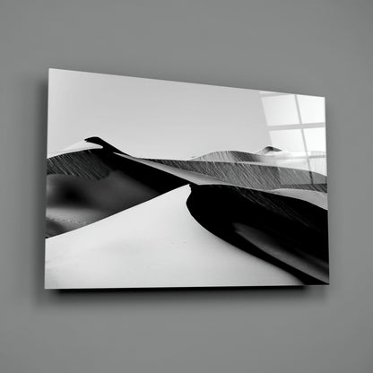 Black and white glass wall art mounted on gray wall, displaying abstract sand dunes with strong shadows and contrast.
