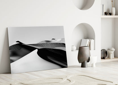 Black and white abstract landscape glass wall art leaning against white wall in minimalist interior setting.