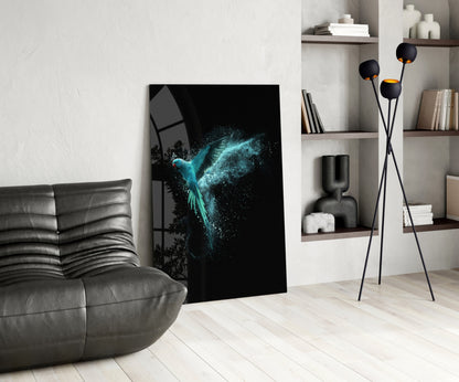 Luminous Parrot Glass Wall Art displayed leaning against white wall in modern living room with gray sofa and shelving.
